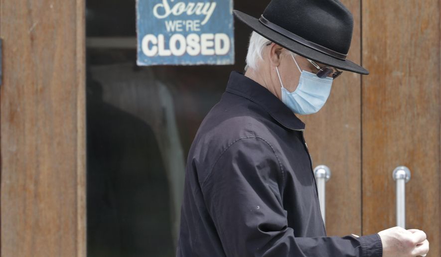 FILE - In this April 29, 2020 file photo, a man walks past a closed business in Shaker Heights, Ohio. Many people consider the Paycheck Protection Program that promised nearly $670 billion in forgivable loans to help companies rehire laid-off workers to already be a success because millions of businesses have gotten the money. But owners and business groups have said loans weren’t getting to companies most in need and it wasn’t arriving fast enough. (AP Photo/Tony Dejak, File)