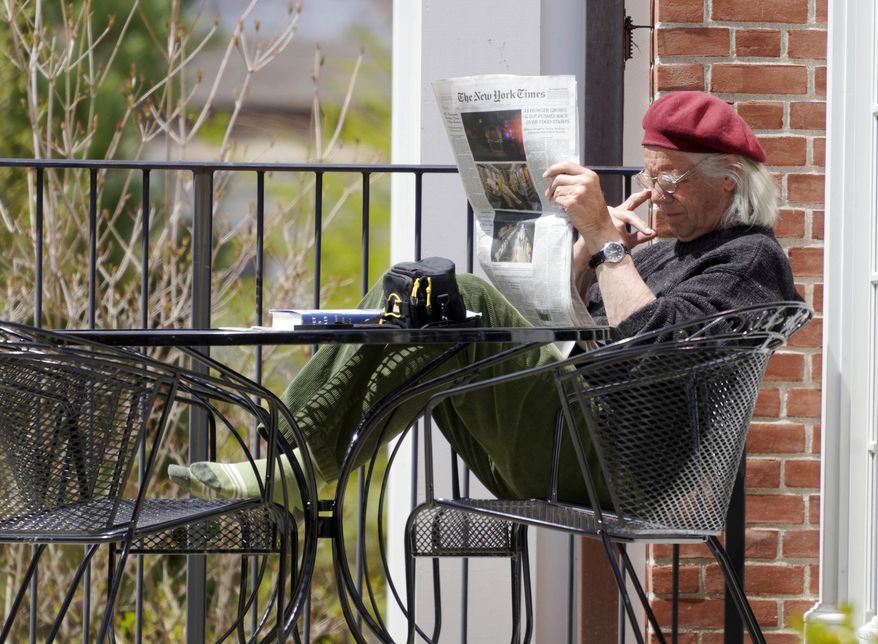 In this Thursday, May 7, 2020, photo, Bob Berkel reads a couple of newspapers during the coronavirus pandemic outside the Stockbridge Library, in Stockbridge, Mass. (Ben Garver/The Berkshire Eagle via AP)