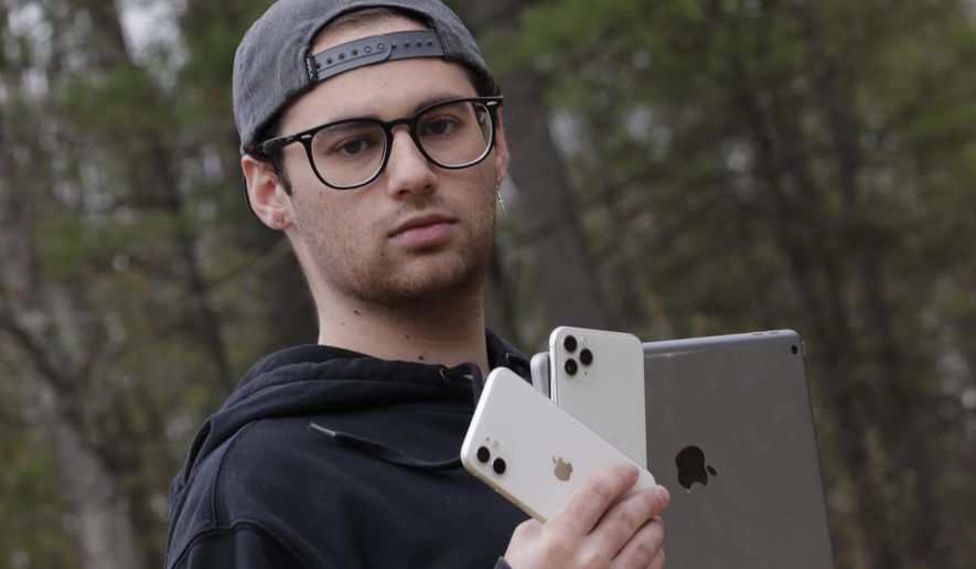 In this Monday, May 4, 2020, photo, Kaya Suner holds up an iPhone and an iPad as he poses for a portrait in Northfield, N.H. Suner, whose parents both work as emergency room physicians in Rhode Island, set up a nonprofit with a former classmate that sends donated digital devices to hospitals and long-term care facilities to help patients communicate with loved ones after the coronavirus pandemic eliminated visitations. (AP Photo/Charles Krupa)