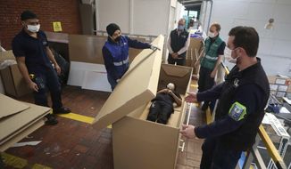 Rodolfo Gomez, to center, and his employees demonstrate how their design of a cardboard box can serve as both a hospital bed and a coffin, designed for COVID-19 patients, in Bogota, Colombia, Friday, May 8, 2020. Gomez said he plans to donate the first units to Colombia&#39;s Amazonas state, and that he will sell others to small hospitals for 87 dollars. (AP Photo/Fernando Vergara)