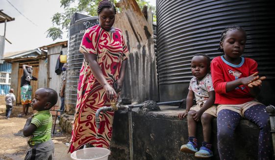In this April 10, 2020, photo, Judith Andeka a widow and mother of five, fetches water with a bucket in the Kibera slum, or informal settlement, of Nairobi, Kenya. Andeka used to earn $2.50 to $4 a day washing clothes in Nairobi’s Kibera, one of the world’s biggest slums. With people not going to work because of restrictions on movement, neighbors can’t afford her services. (AP Photo/Brian Inganga)