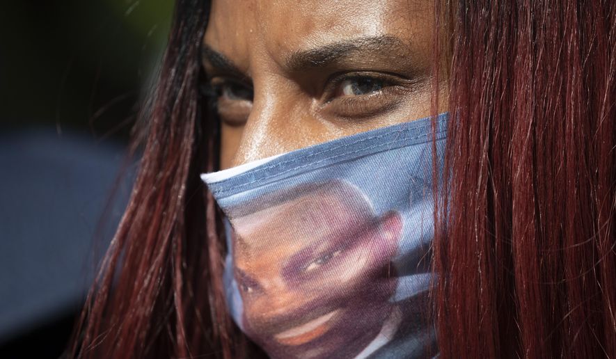 FILE- In this May 8, 2020 file photo, a woman wears a face covering with the likeness of shooting victim Ahmaud Arbery printed on it during a rally to protest Arbery's killing, in Brunswick Ga. T. Georgia’s attorney general has asked the U.S. Department of Justice to investigate the handling of the killing of Ahmaud Arbery. Authorities say Arbery, a black man, died at the hands of two white men in February near the coastal city of Brunswick as he ran through a neighborhood. (AP Photo/John Bazemore, File)