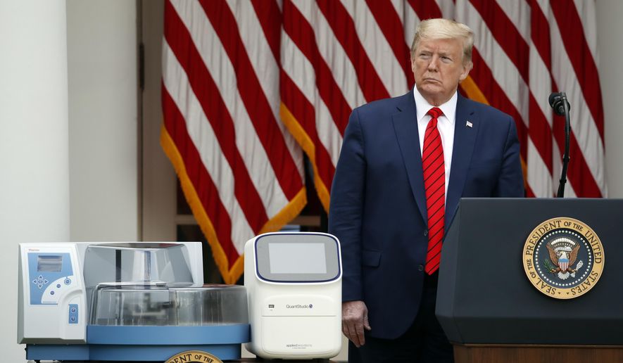 President Donald Trump listens during a briefing about the coronavirus in the Rose Garden of the White House, Monday, May 11, 2020, in Washington. In the foreground are testing machines manufactured by Thermo Fisher Scientific. (AP Photo/Alex Brandon)