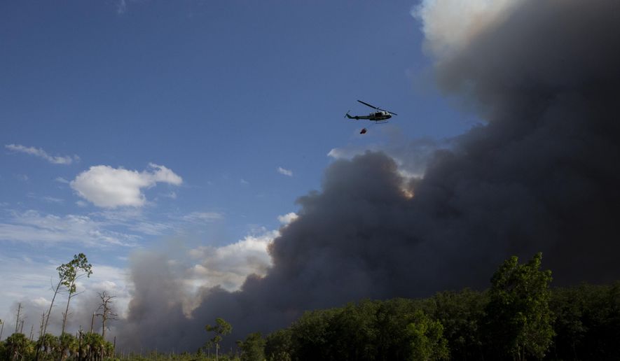 A helicopter, carrying a bucket, flies near a brush fire in Golden Gate Estates, Fla., on Wednesday, May 13, 2020. Crews worked to contain four brush fires totaling about 400 acres and threatening 30 homes in the Estates. (Jon Austria/Naples Daily News via AP)