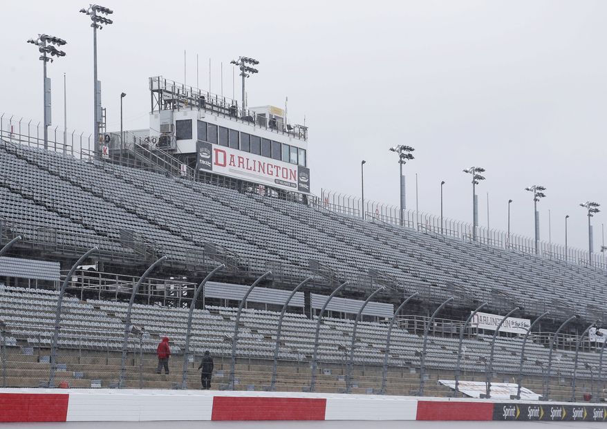  In this Sept. 2, 2016, file photo, workers walk along the grandstands in the rain at Darlington Raceway after weather forced NASCAR to call off qualifying for the Sprint Cup and XFinity series auto races. NASCAR says it will resume its season without fans present starting May 17 at Darlington Raceway in South Carolina. (AP Photo/Terry Renna, File)  **FILE**