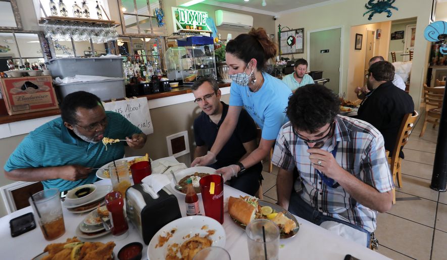 Waitress Gina Lauricella serves customers indoors, for the first time since the state shutdown, at Charles Seafood Restaurant in Harahan, La., Friday, May 15, 2020. Once a hot spot for coronavirus infections, Louisiana is officially easing up Friday on economically devastating business closures and public gathering restrictions that Gov. John Bel Edwards credits with slowing the spread of the virus. (AP Photo/Gerald Herbert)