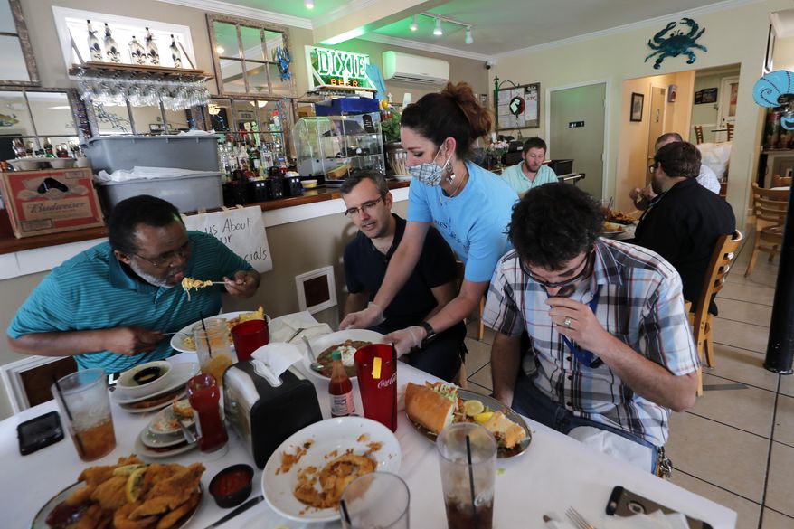 Waitress Gina Lauricella serves customers indoors, for the first time since the state shutdown, at Charles Seafood Restaurant in Harahan, La., Friday, May 15, 2020. Once a hot spot for coronavirus infections, Louisiana is officially easing up Friday on economically devastating business closures and public gathering restrictions that Gov. John Bel Edwards credits with slowing the spread of the virus. (AP Photo/Gerald Herbert)