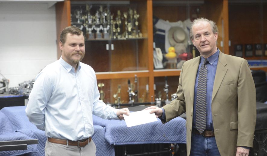 In this Thursday, May 14, 2020 photo, Charles Womack, right, delivers a check for $50,000 from the Womack Foundation to George Washington High Schools director of bands Cody Kesling in the school's band room in Danville, Va. (Parker Cotton/Danville Register & Bee via AP)