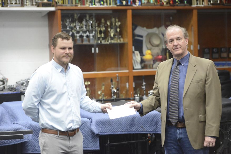 In this Thursday, May 14, 2020 photo, Charles Womack, right, delivers a check for $50,000 from the Womack Foundation to George Washington High Schools director of bands Cody Kesling in the school's band room in Danville, Va. (Parker Cotton/Danville Register & Bee via AP)