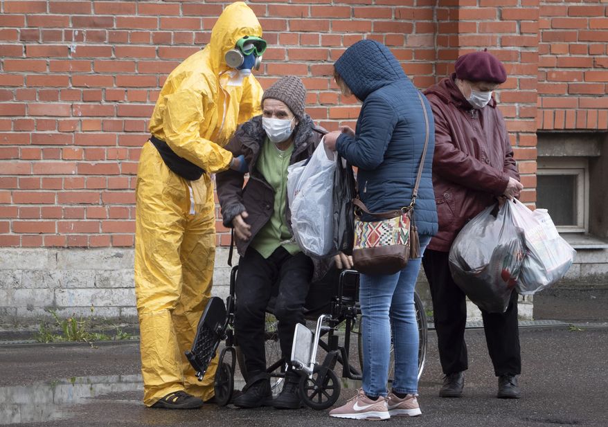 A medical worker wearing protective clothing helps a woman out of her wheelchair as she leaves after receiving treatment at a hospital for COVID-19 patients in St. Petersburg, Russia, Monday, May 18, 2020. (AP Photo/Dmitri Lovetsky)
