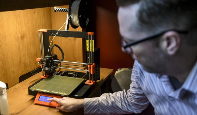 In this Tuesday, May 5, 2020 photo, Mitchell Olson resets a 3D printer to make a new batch of COVID-19 testing swabs at his home in Sioux Falls, S.D. (Abigail Dollins/The Argus Leader via AP)