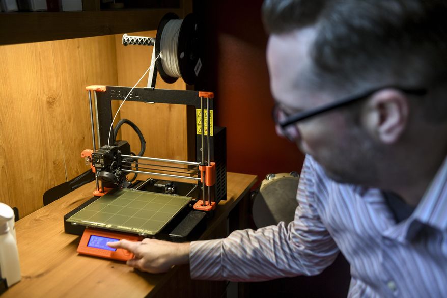 In this Tuesday, May 5, 2020 photo, Mitchell Olson resets a 3D printer to make a new batch of COVID-19 testing swabs at his home in Sioux Falls, S.D. (Abigail Dollins/The Argus Leader via AP)