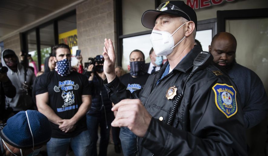 A police officer addresses supporters of Atilis Gym co-owners Frank Trumbetti, center, Ian Smith, left, outside their gym in Bellmawr, N.J., Monday, May 18, 2020. The gym in New Jersey reopened for business early Monday, defying a state order that shut down nonessential businesses to help stem the spread of the coronavirus. (AP Photo/Matt Rourke)