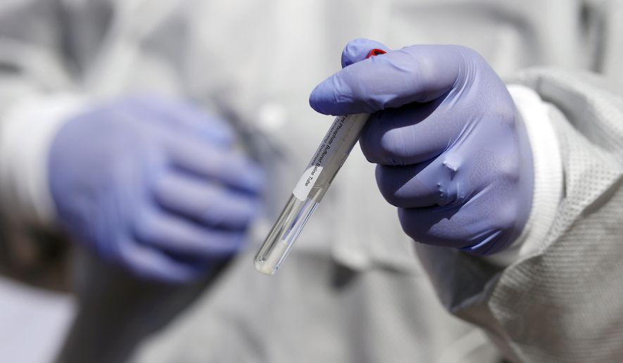 The swab used for a nasal test for the new coronavirus on Colorado Governor Jared Polis, not in the picture, is held by registered nurse Stephanie Campbell during a news conference outside the Stride Community Health Center Monday, May 18, 2020, in Wheat Ridge, Colo. (AP Photo/David Zalubowski)