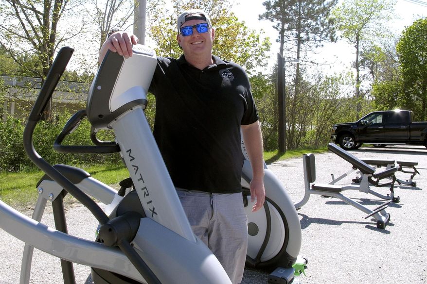 Sean Manovill, owner of Club Fitness of Vermont, poses with exercise equipment he moved outside so the Rutland, Vt., gym could reopen on Tuesday, May 19, 2020. The Vermont attorney general sued him and the fitness center for being open on Friday, which he said was against the state rules amid the coronavirus outbreak, and judge granted an order to temporarily close it. (AP Photo/Lisa Rathke)