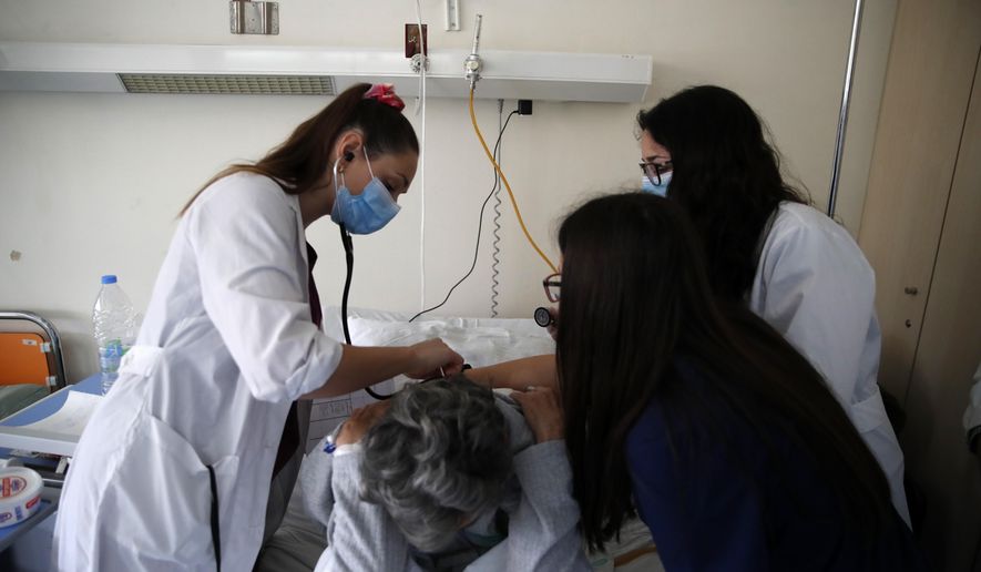 In this photo taken on Thursday, May 7, 2020, medical students Afroditi Gerodimontaki, left, Michaella Alexandrou, center, and Dimitra Siakalli examine a patient at the Pathological Clinic of Sotiria Hospital in Athens. Greece's main hospital for the treatment of COVID-19 is also the focus of a hands-on training program for dozens of medical students who volunteered to relieve hard-pressed doctors from their simpler duties while gaining a close peek at the front lines of a struggle unmatched in modern medical history. (AP Photo/Thanassis Stavrakis)