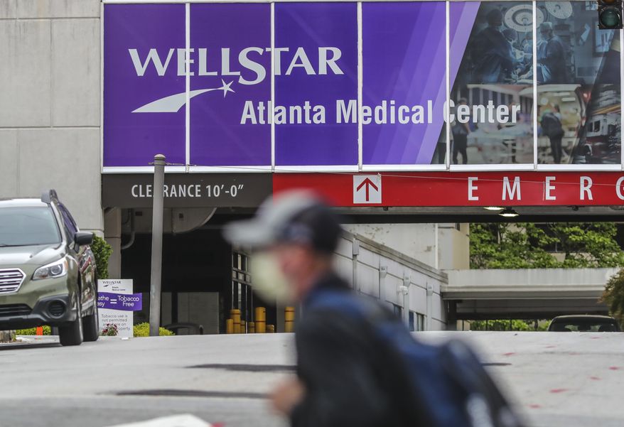 A masked man passes Wellstar Atlanta Medical Center on Boulevard in Atlanta on Wednesday, May 20, 2020 after the Wellstar Health System announced Tuesday that it would furlough more than 1,000 employees across its hospital network. The system cited a drop in patient volume due to the coronavirus pandemic as the reason for the financial measures. (John Spink/Atlanta Journal-Constitution via AP)