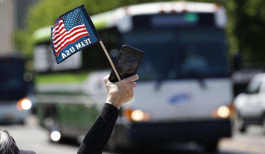 FILE - In this May 13, 2020, file photo, tour guide Barbara Western waves a flag in support of bus and motor coach operators circling National Mall in Washington during a rally to raise awareness of the industry in the wake of the coronavirus outbreak. America's private buses are ground to a halt, and members of the industry say they need federal assistance to help the country get back to work and play. (AP Photo/Patrick Semansky, File)