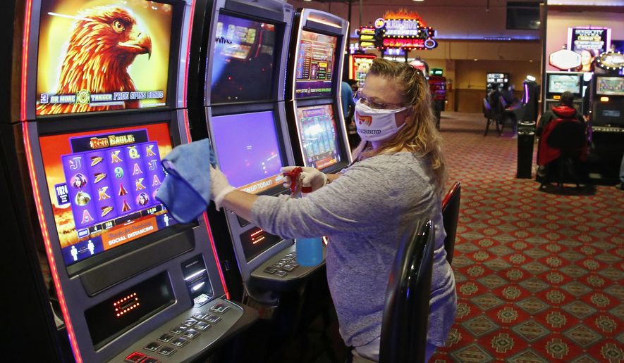 Katie Blevins, manager on duty, disinfects slot machines Tuesday, May 12, 2020, at Thunderbird Casino in Norman, Okla. The Casino, operated by the Absentee Shawnee Tribe, has reopened for business with about one-third of capacity allowed and social distancing guidelines. Guests and employees are required to wear masks. (AP Photo/Sue Ogrocki)