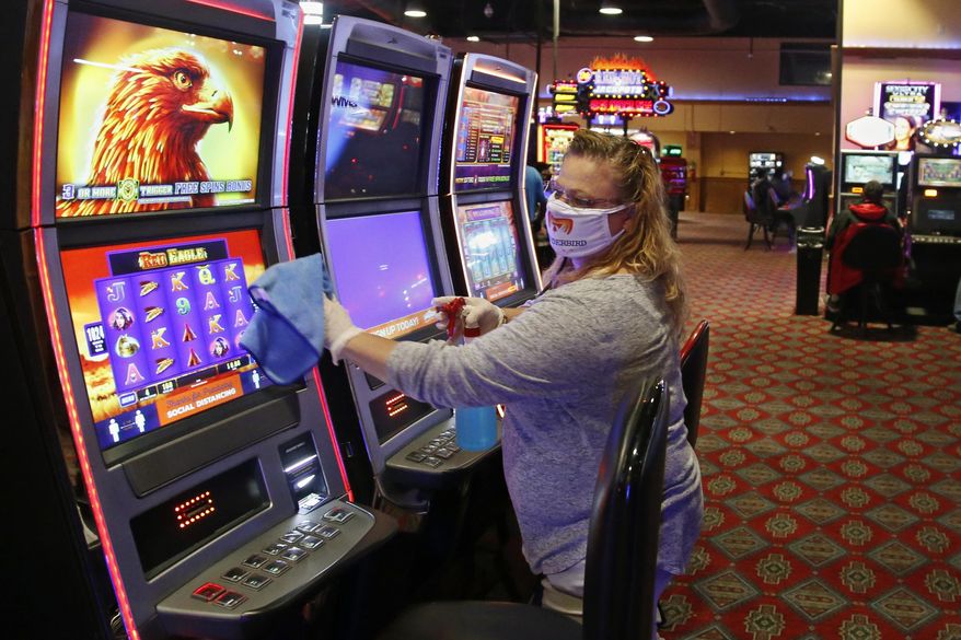 Katie Blevins, manager on duty, disinfects slot machines Tuesday, May 12, 2020, at Thunderbird Casino in Norman, Okla. The Casino, operated by the Absentee Shawnee Tribe, has reopened for business with about one-third of capacity allowed and social distancing guidelines. Guests and employees are required to wear masks. (AP Photo/Sue Ogrocki)
