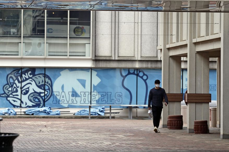 In this March 18, 2020, photo, a pedestrian walks through campus at the University of North Carolina in Chapel Hill, N.C. The University of North Carolina and North Carolina State University announced plans Thursday, May 21 to resume in-person classes in August and end fall semesters early as a precaution against spreading COVID-19. (AP Photo/Gerry Broome) **FILE**