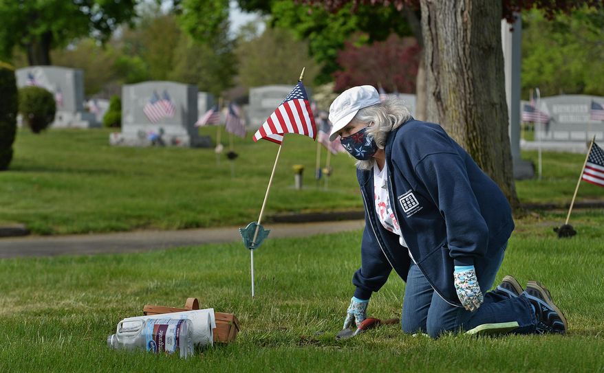 Carolyn Lauer takes a break from tending a gravestone to talk with her sister Nancy Kissinger, Wednesday, May 20, 2020, at Calvary Cemetery in Millcreek Township, Erie County, Pennsylvania. The siblings were cleaning family grave markers in advance of Memorial Day. While doing the annual work, Lauer, 67, of Lawrence Park Township, Erie County, wore an American flag-themed face mask that she made herself. "It's the most comfortable mask I have," said Lauer. "And I like the flags." (Christopher Millette/Erie Times-News via AP)