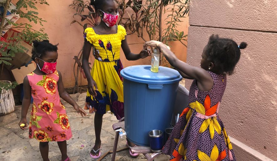 In this May 21, 2020, photo, the Larson sisters wash their hands inside the gate at their home in Dakar, Senegal. The girls were adopted from Sierra Leone after their father and other relatives died of Ebola. (AP Photo/Krista Larson)