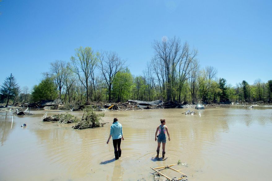 Kendra Tucker, left, and her sister Melissa McCann, both of Sanford, wade into flood waters as they work to uncover lost family heirlooms and belongings, Thursday, May 21, 2020, in Sanford, Mich. Scores of displaced people are staying in shelters after flooding overwhelmed two dams, submerged homes and washed out roads in Central Michigan. (Jake May/MLive.com/The Flint Journal via AP)