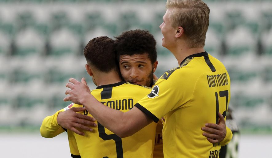 Dortmund's Achraf Hakimi, left, celebrates with Jadon Sancho and Erling Haaland, right, after scoring his side's second goal during the German Bundesliga soccer match between VfL Wolfsburg and Borussia Dortmund in Wolfsburg, Germany, Saturday, May 23, 2020. The German Bundesliga is the world's first major soccer league to resume after a two-month suspension because of the coronavirus pandemic. (AP Photo/Michael Sohn, Pool)