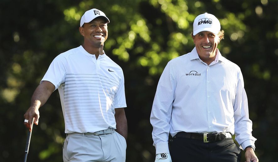 In this April 3, 2018, file photo, Tiger Woods, left, and Phil Mickelson share a laugh on the 11th tee box while playing a practice round for the Masters golf tournament at Augusta National Golf Club in Augusta, Ga. The next match involving Tiger Woods and Phil Mickelson involves a $10 million donation for COVID-19 relief efforts, along with plenty of bragging rights in a star-powered foursome May 24 at Medalist Golf Club. Turner Sports announced more details Thursday, May 7, 2020, for “The Match: Champions for Charity,” a televised match between Woods and Peyton Manning against Mickelson and Tom Brady. (Curtis Compton/Atlanta Journal-Constitution via AP, File)  **FILE**