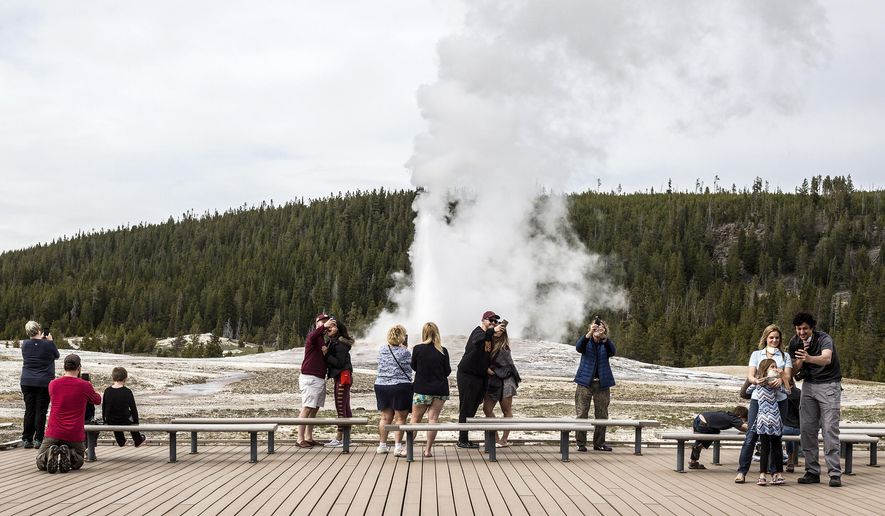 In this Monday, May 18, 2020 photo, visitors watch as Old Faithful erupts on the day the park partially reopened after a two-month shutdown due to the coronavirus pandemic, at Yellowstone National Park, Wyo. Officials at Yellowstone and other national parks plan to let tourists mostly police themselves and not intervene much to enforce social distancing. (Ryan Dorgan/Jackson Hole News &amp;amp; Guide via AP)
