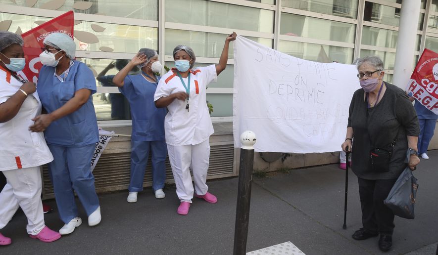 An elderly woman walks past employees demonstrating outside a nursing home of the Korian group, one of the market leaders in the lucrative industry of providing care and assisted living facilities for older adults, Monday, May 25, 2020 in Paris. In France, the group is facing several lawsuits filed by families who have lost loved ones during the coronavirus pandemic that has caused thousands of deaths in French care homes. (AP Photo/Thibault Camus)
