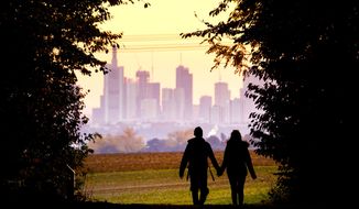 A young couple walks through a forest with the Frankfurt skyline in the background near Frankfurt, Germany, on Oct. 21, 2018. (Associated Press) **FILE**