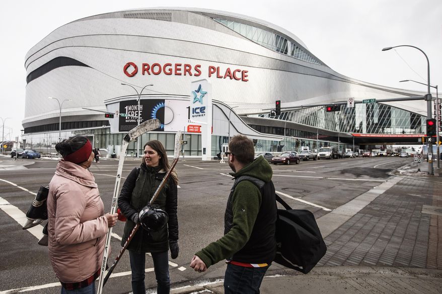 In this March 12, 2020, file photo, people talk outside Rogers Place, the home ice of the Edmonton Oilers, in Edmonton, Alberta. Rogers Place is one of the possible locations the NHL has zeroed in on to host playoff games if it can return amid the coronavirus pandemic. The league will ultimately decide on two or three locations for games, with government regulations, testing and COVID-19 frequency among the factors for the decision that should be coming within the next three to four weeks.(Jason Franson/The Canadian Press via AP) ** FILE **