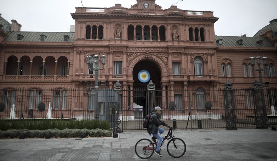 FILE - In this May 21, 2020, file photo, a man rides a bicycle in front of the government house during a government-ordered lockdown to curb the spread of COVID-19 in Buenos Aires, Argentina. Even amid a global pandemic, there’s no sign that corruption is slowing down in Latin America. From Argentina to Panama, a number of officials have been forced to resign as reports of possibly fraudulent purchases of ventilators, masks and medical supplies proliferate. (AP Photo/Natacha Pisarenko, File)