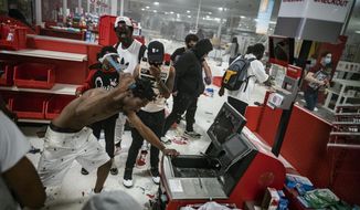 In this Wednesday, May 27, 2020 photo, a looter uses a claw hammer as he tries to break in to a cash register at a Target store in Minneapolis. Rioters ignited fires and looted stores all over the city, as peaceful protests turned increasingly violent in the aftermath of the death of George Floyd. (Richard Tsong-Taatarii/Star Tribune via AP)