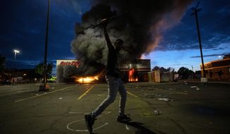 A man poses for a photo in the parking lot of an AutoZone store in flames, while protesters hold a rally for George Floyd in Minneapolis on Wednesday, May 27, 2020. Violent protests over the death of the black man in police custody broke out in Minneapolis for a second straight night Wednesday, with protesters in a standoff with officers outside a police precinct and looting of nearby stores. (Carlos Gonzalez/Star Tribune via AP)