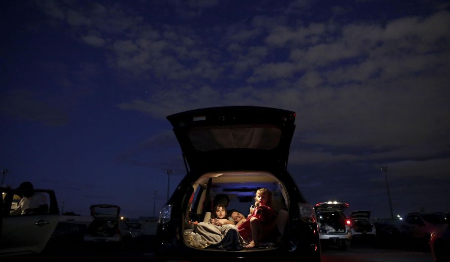 A family watches a movie from the back of their car at a drive-in movie theater where drivers must leave one space empty between them amid the new coronavirus pandemic in Brasilia, Brazil, Saturday, May 23, 2020. The drive-in is 47 years old and one of the only such open-air facilities in operation in Brazil. (AP Photo/Eraldo Peres)