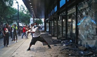 A protester smashes a window at the CNN center Friday, May 29, 2020, in Atlanta. They carried signs and chanted their messages of outrage over the death of George Floyd in Minneapolis. (Alyssa Pointer/Atlanta Journal-Constitution via AP)