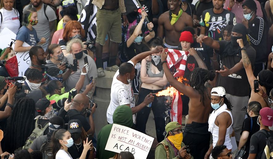 Demonstrators light an American flag on fire during a protest, Friday, May 29, 2020 in Atlanta. The protest started peacefully earlier in the day before demonstrators clashed with police. (AP Photo/Mike Stewart)