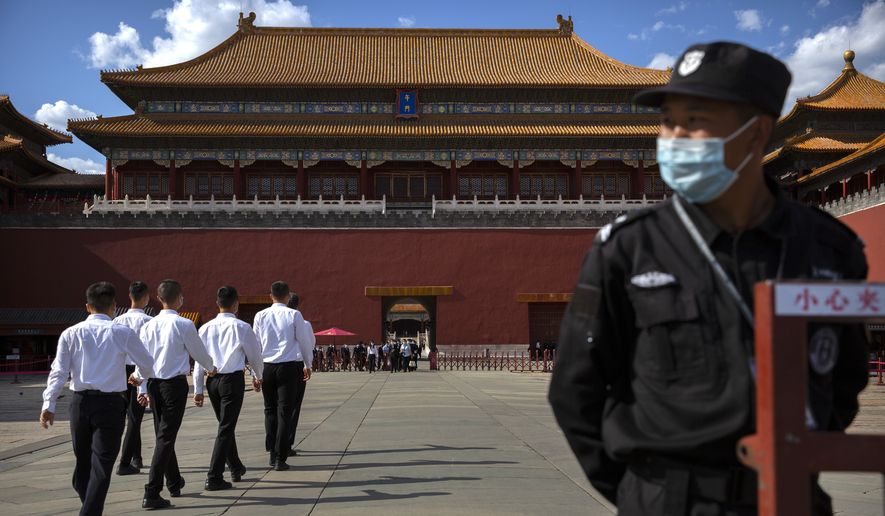 A security officer wearing a face mask to protect against the COVID-19 coronavirus stands guard as plainclothes personnel march in formation outside the entrance to the Forbidden City in Beijing, Wednesday, May 27, 2020. The Chinese People's Political Consultative Conference (CPPCC) concluded its session in Beijing on Wednesday, part of the annual meetings of China's two top legislative bodies. (AP Photo/Mark Schiefelbein)