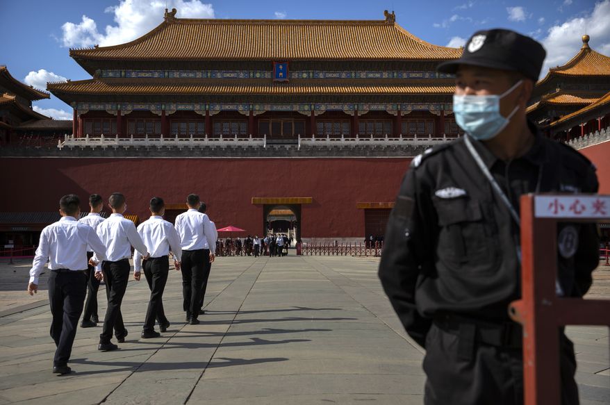 A security officer wearing a face mask to protect against the COVID-19 coronavirus stands guard as plainclothes personnel march in formation outside the entrance to the Forbidden City in Beijing, Wednesday, May 27, 2020. The Chinese People's Political Consultative Conference (CPPCC) concluded its session in Beijing on Wednesday, part of the annual meetings of China's two top legislative bodies. (AP Photo/Mark Schiefelbein)