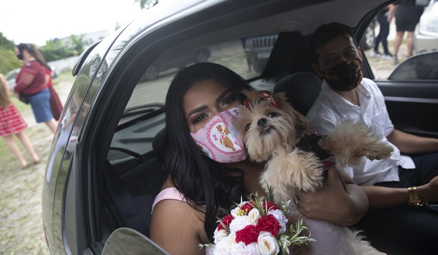 Wearing masks to prevent the spread of the new coronavirus, Erica da Conceicao and Joao Blank ride in the back seat of a car for a drive-thru wedding at the registry office in the neighborhood of Santa Cruz, Rio de Janeiro, Brazil, Thursday, May 28, 2020. A Brazilian notary public hovering outside the car presided over Thursday&#39;s ceremony. The drive-thru marriage wasn’t the romantic vision the Blanks had imagined, but it is one of few possibilities in the era of COVID-19. (AP Photo/Silvia Izquierdo)