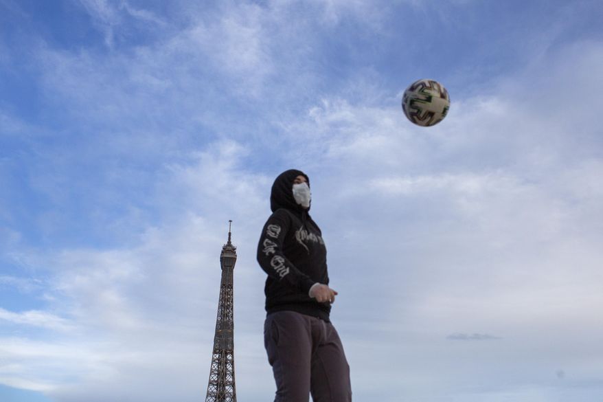 A young man wears a mask to protect against the spread of the coronavirus as he plays with a soccer ball along the Trocadero square close to the Eiffel Tower in Paris, Saturday May 2, 2020 in Paris. France continues to be under an extended stay-at-home order until May 11 in an attempt to slow the spread of the COVID-19 pandemic. (AP Photo/Rafael Yahgobzadeh)