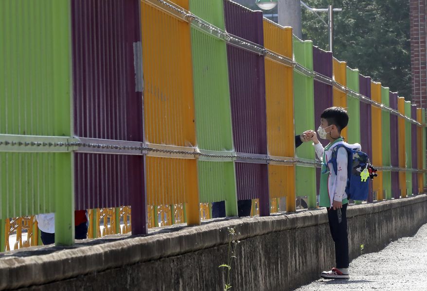 A pupil wearing a face mask to help protect against the spread of the new coronavirus holds his mother's hand through a fence as he arrives at the Ochi Elementary School in Gwangju, South Korea, Friday, May 29, 2020. (Park Chul-hong/Yonhap via AP)