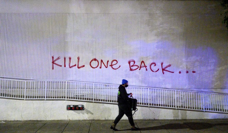 A demonstrator passes graffiti in Oakland, Calif., on Friday, May 29, 2020, while protesting the Monday death of George Floyd, a handcuffed black man in police custody in Minneapolis. A federal protective services officer was fatally shot Friday night, the FBI announced Saturday morning. (AP Photo/Noah Berger)