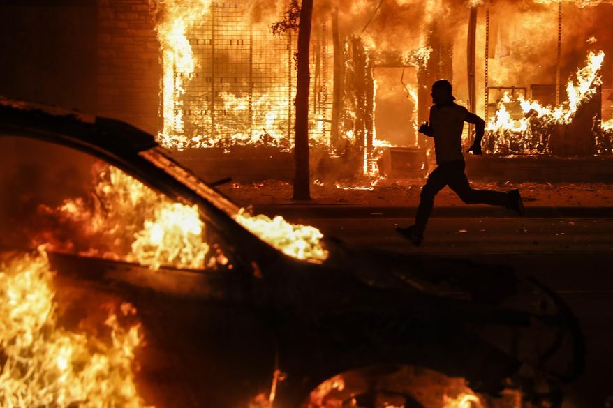 A protester runs past burning cars and buildings on Chicago Avenue, Saturday, May 30, 2020, in St. Paul, Minn. Protests continued following the death of George Floyd, who died after being restrained by Minneapolis police officers on Memorial Day. (AP Photo/John Minchillo)