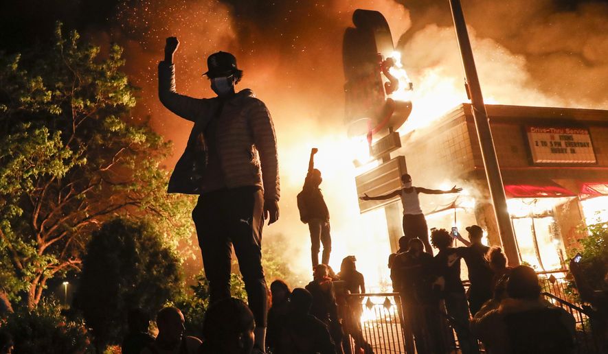 Protestors demonstrate outside of a burning fast food restaurant, early Friday, May 29, 2020, in Minneapolis. Protests over the death of George Floyd, a black man who died in police custody Monday, broke out in Minneapolis for a third straight night. (AP Photo/John Minchillo)
