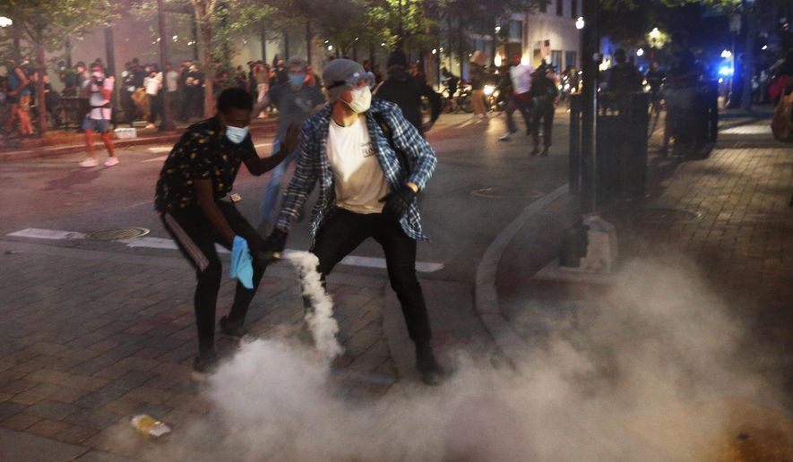 A protester tosses a smoke bomb towards police during a third night of unrest Sunday May 31, 2020, in Richmond, Va. Gov. Ralph Northam issued a curfew for this evening. The smoke bomb was ignited by a protester. (AP Photo/Steve Helber)