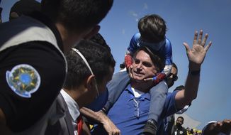 Brazil&#39;s President Jair Bolsonaro carries a boy on his back as he greets supporters gathered outside the presidential palace in Brasilia, Brazil, Sunday, May 31, 2020. (AP Photo/Andre Borges)